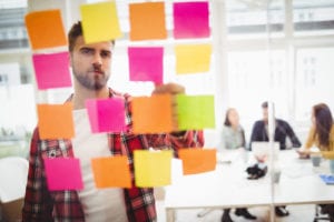 A Manager uses sticky notes on a glass wall to work through Business Process Re-Engineering.