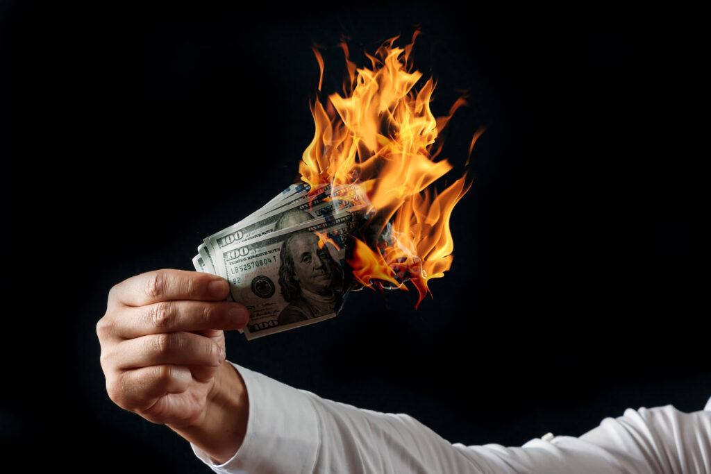 A man holds a burning handful of $100 bills