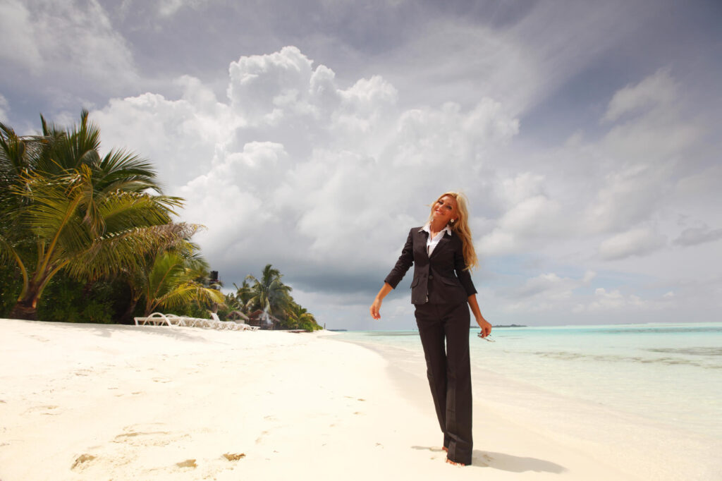 A professional woman dressed in business attire enjoys a sandy beach
