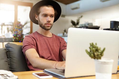 A young man, and remote worker, types on a laptop depicting that he works on a virtual team