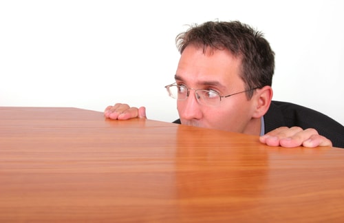 A timid leader hides behind his desk depicting avoiding employee accountability