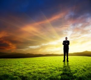 A businessman stands in a green field with a sunset behind him. Leadership Tips: Starting Your Career