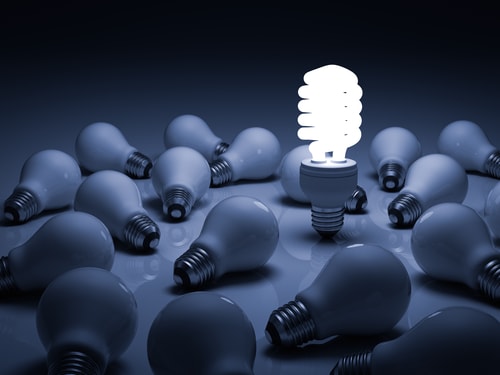 A photo of one lightbulb lit among an array of unlit bulbs