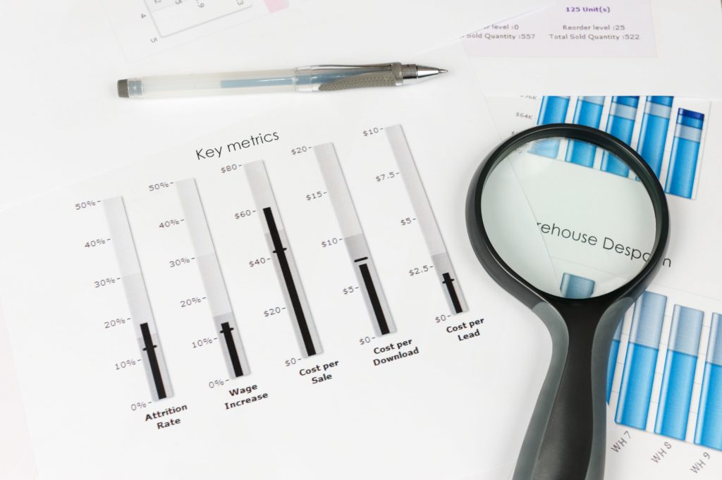 a chart of numbers and graphs are on a desk with a magnifying glass nearby.