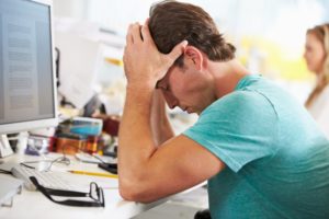 An employee rubs his face with his hands depicting stress in the workplace