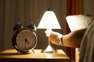 A man turns off his bedside light near his alarm clock