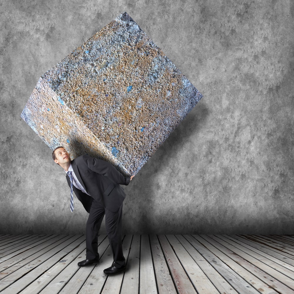 businessman carrying a large stone cube and not utilizing effective delegation skills