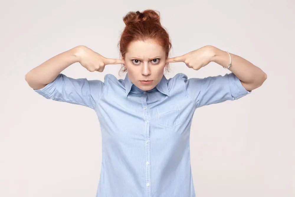 A stern red-haired woman plugs her ears to help control her temper and emotions at work
