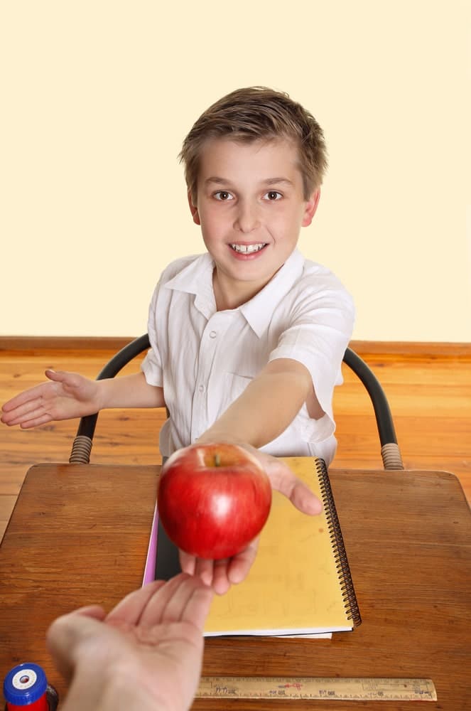 A young student handing an apple to a teacher which signifies avoid employee favoritism at work