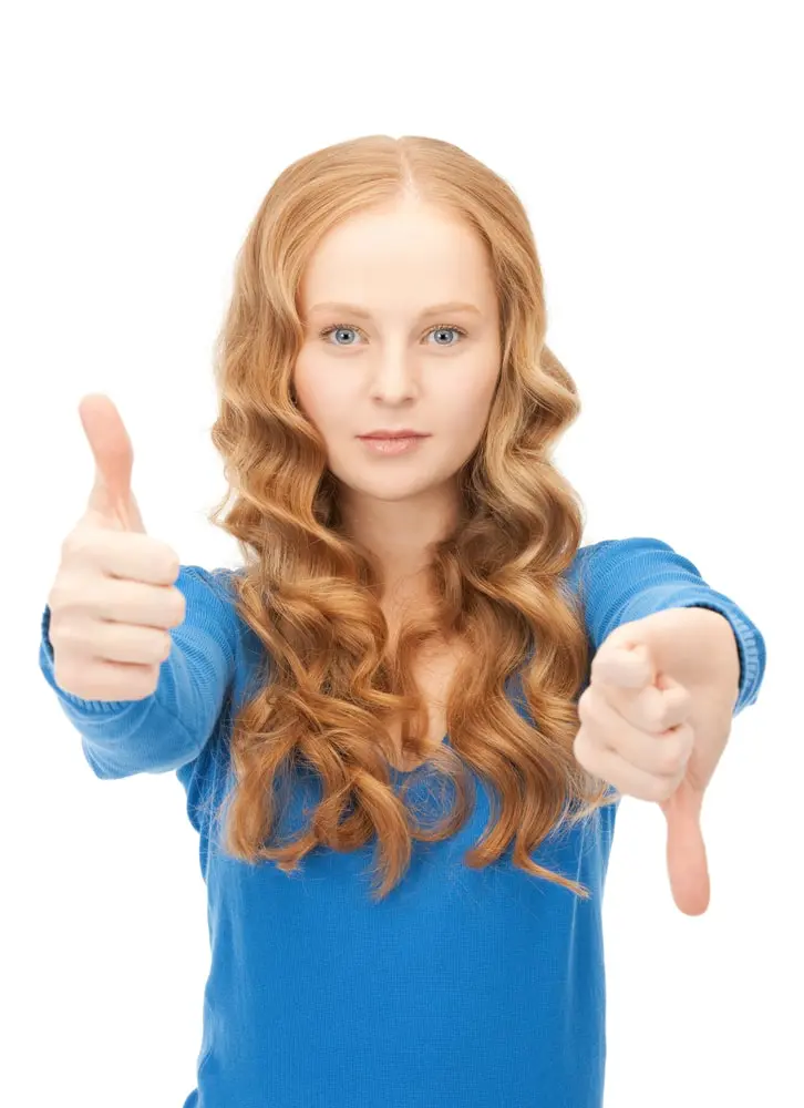 A photo of a red-haired young woman showing thumbs up and thumbs down which is typical when you have unconscious bias in interviewing