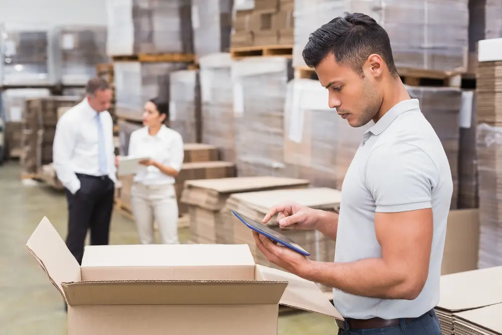 A male warehouse worker verifies retail inventory management and data in a warehouse