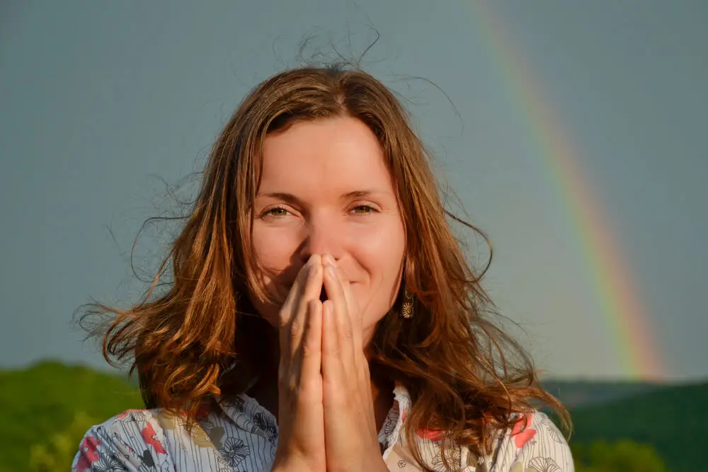 A thoughtful woman smiling behind her praying hands that signify mindfulness in the workplace