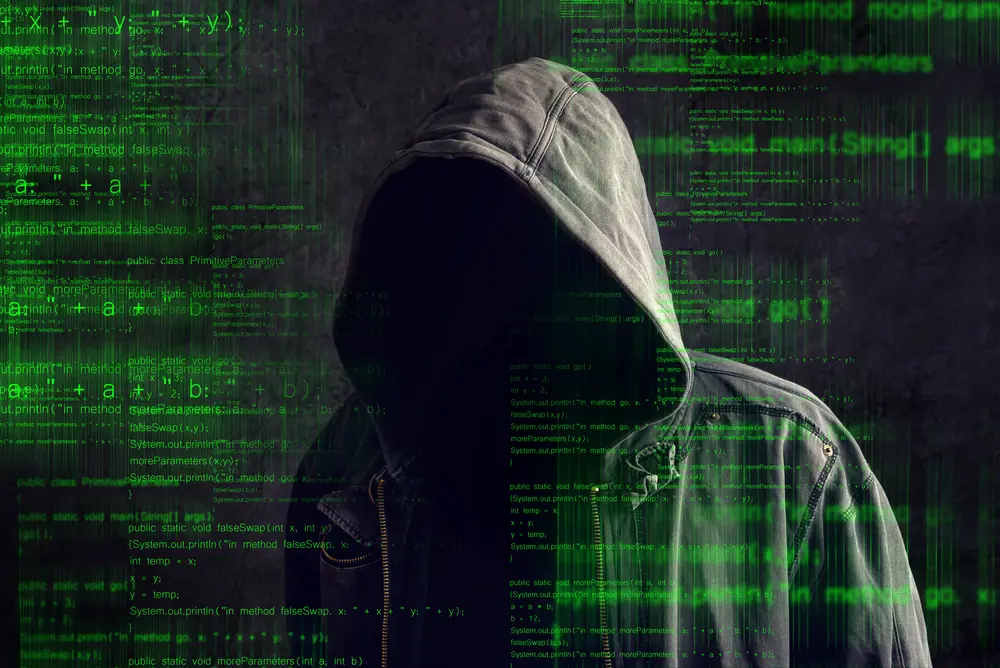 a photo of hooded cyber thief on a background of computer code