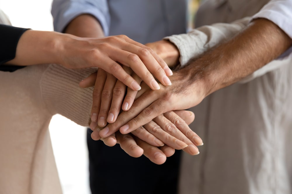 Three teammates touch their hands together signifying leadership and accountability in the workplace