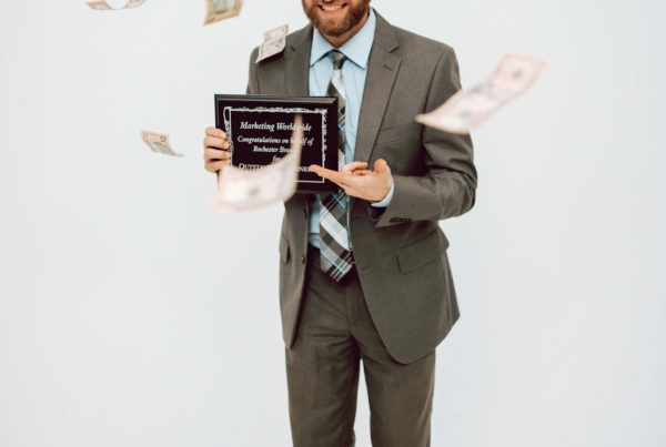A well-dressed employee is holding a plaque and showered in currency, depicting that he is an A player.