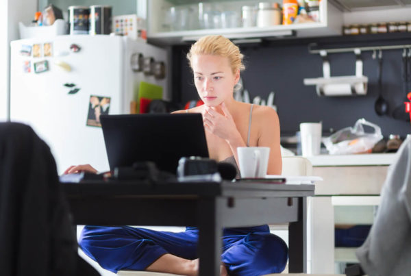 A young casually dressed woman is sitting cross leg while working from home on a laptop