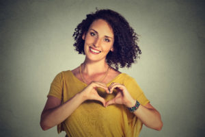 A young professional woman makes a heart sign indicating humanity and kindness