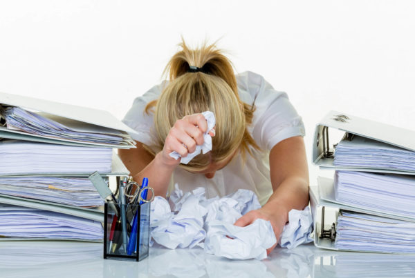 A woman entrepreneur is face down on her desk surrounded by stacks of books and crumpled papers