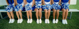 Seven cheerleaders sit on a bench with their pom-poms