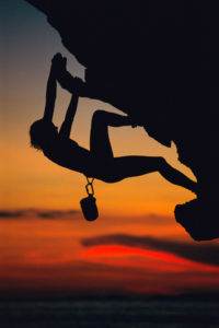 An athletic inverted young woman is climbing up a mountain
