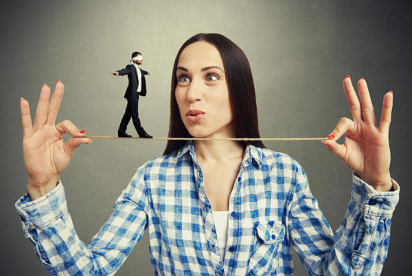 a woman holds a tightrope in between her hands and a small businessman walks across the rope.