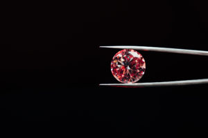 A red diamond is held in a tweezer depicting value instead of price