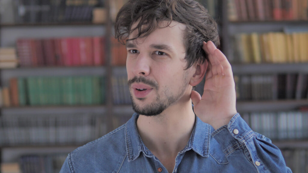 A young worker holds his hand behind his ear to depict effective listening.