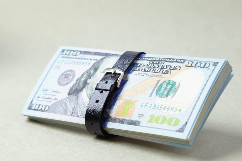 A belt tightens around a stack of currency depicting a business downsizing effort