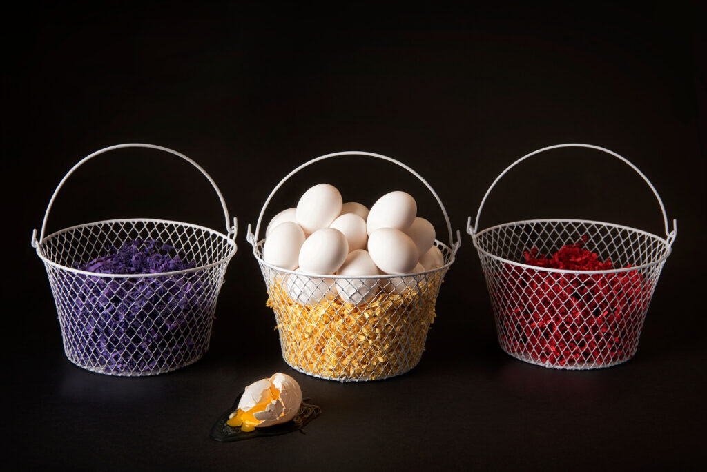 A photo of three egg baskets with all of the eggs in the center basket depicting a diversification strategy