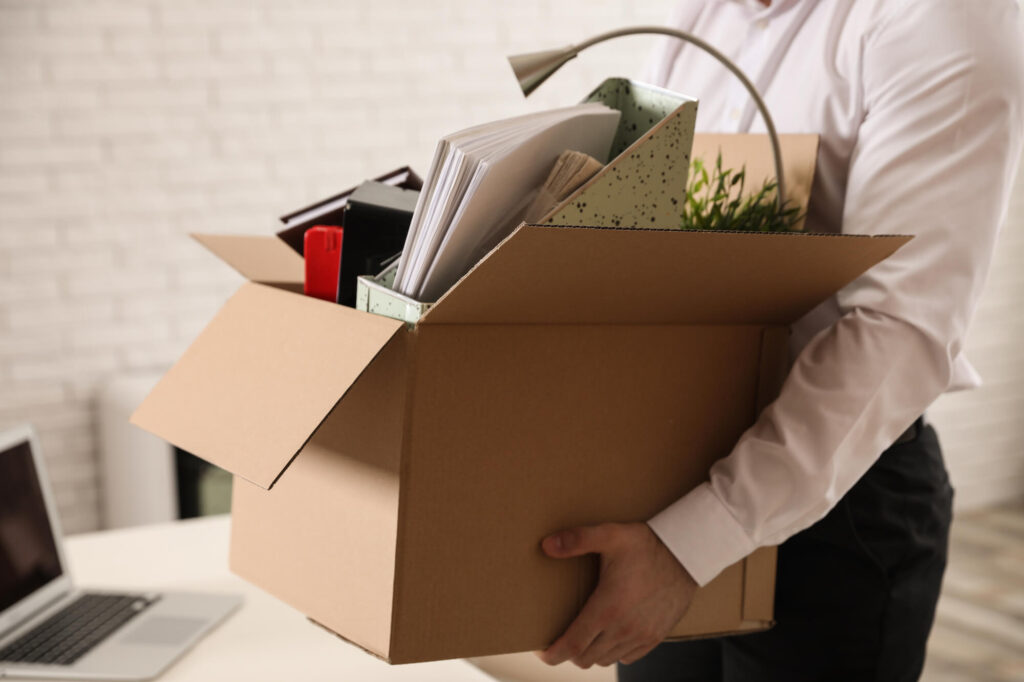 A fired worker carries a box of belongings depicting a company exit interview