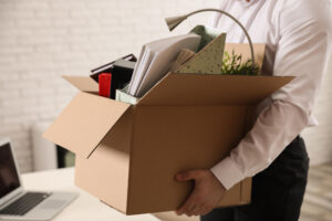 A fired worker carries a box of belongings depicting a company exit interview