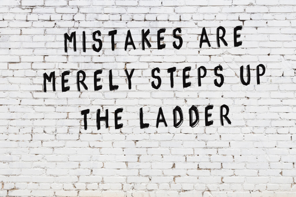 A sign is painted on a white brick wall that reads "mistakes are merely steps up the ladder"