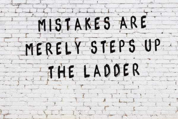 A sign is painted on a white brick wall that reads "mistakes are merely steps up the ladder"