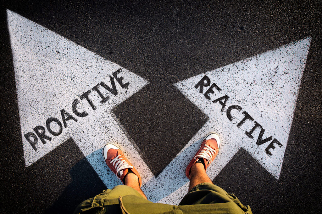 A man stands on two arrows. One says proactive, and the other says reactive