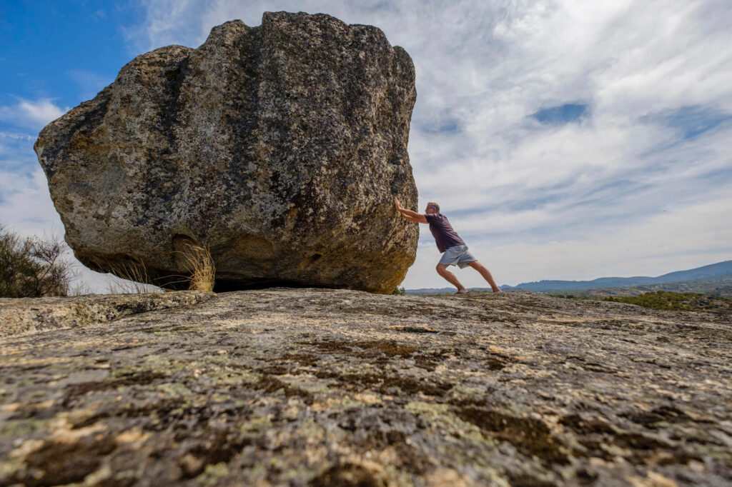 A photo of a man pushing a giant boulder up a mountain.