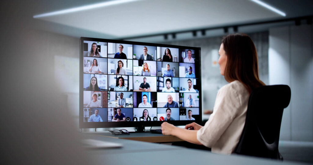 A businesswoman looks at her oversized monitor and can see 25 of her work colleagues.