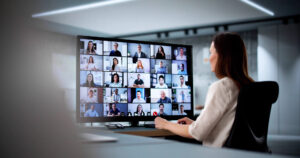 A businesswoman looks at her oversized monitor and can see 25 of her work colleagues.