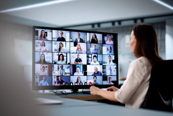 A businesswoman looks at her oversized monitor and can see 25 of her work colleagues.