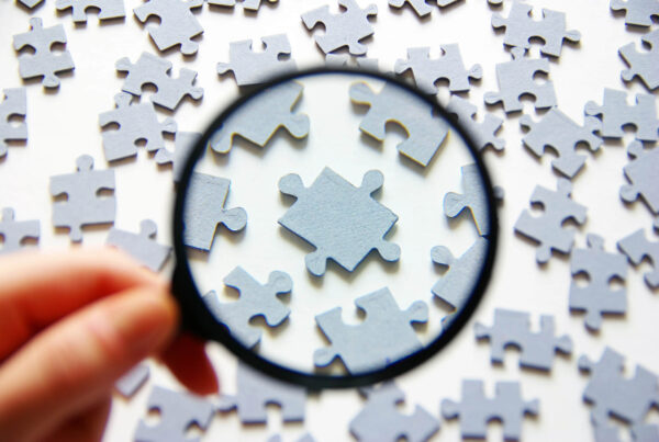 A man holds a magnifying glass on a tabletop full of puzzle pieces