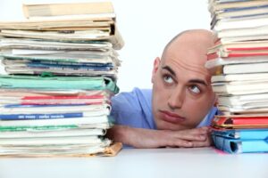 A photo of a tired businessman resting his chin between two huge stacks of files