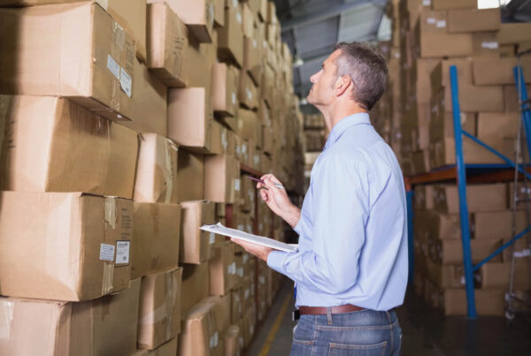 A manager tries to manually inventory a full warehouse with a clipboard and pent