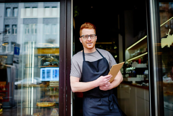 A young red headed baker stands in the doorway of his new shop